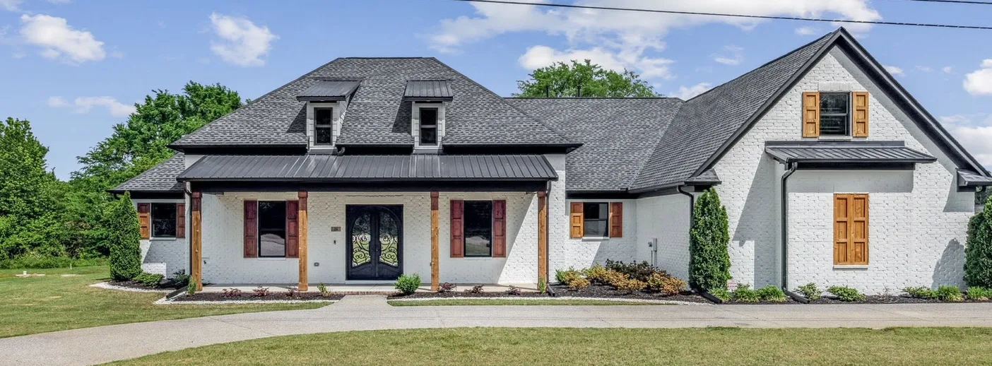 A white brick home with a covered porch and a gabled wing